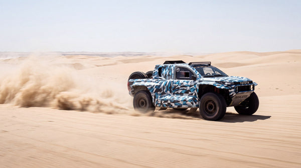 Render of a camouflaged GAZOO Racing Hilux rally raid prototype crossing desert dunes