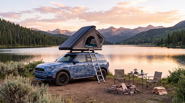 Mini Countryman in blue camouflage with a rooftop tent, parked by a lake at sunset