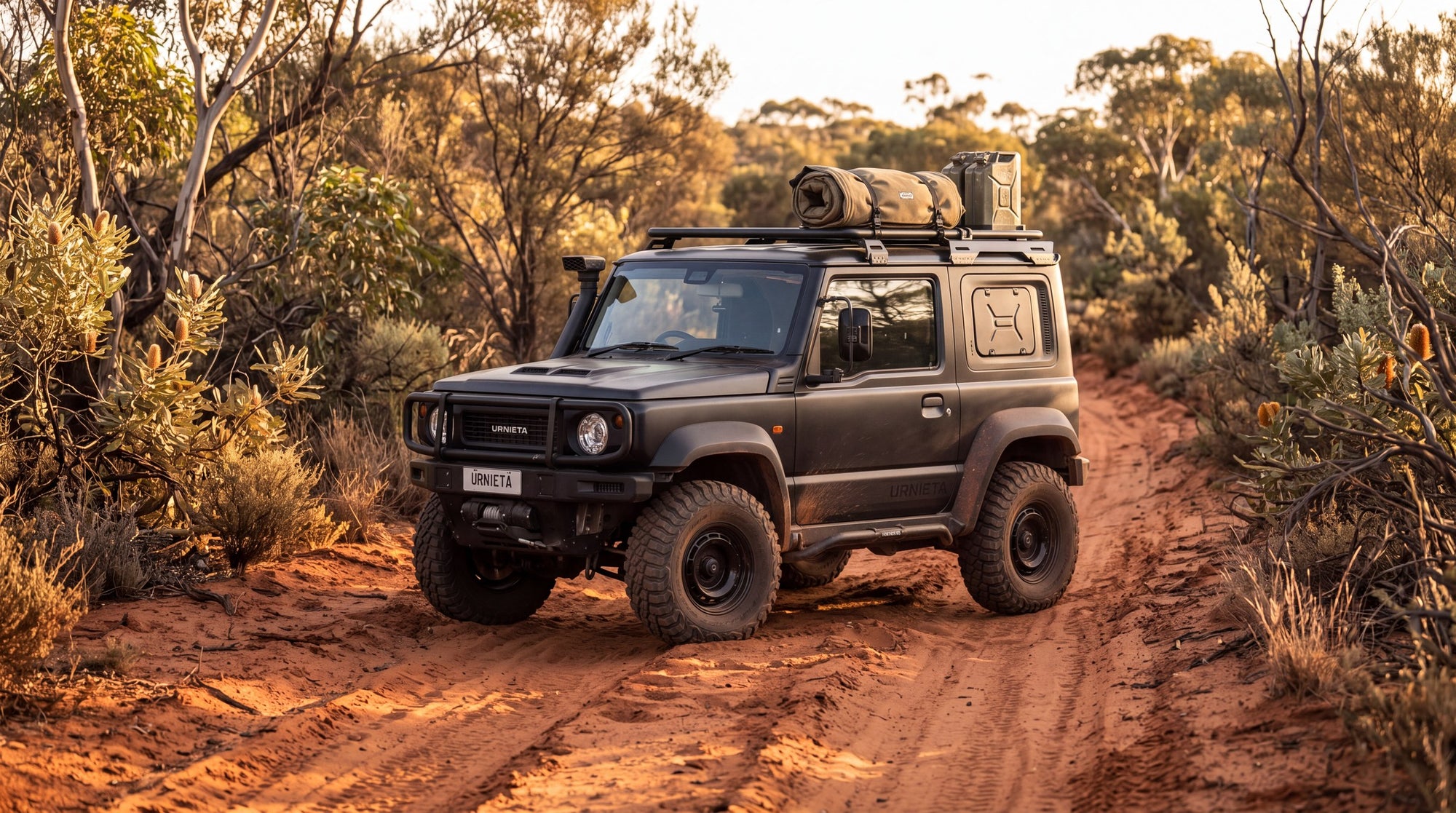 Suzuki Jimny fitted with a Urnieta bull bar, snorkel and roof rack on a red dirt track in the bush