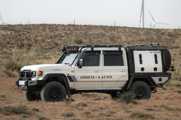 White Toyota LandCruiser 79 Series dual cab with a tray, canopy, safari roof cage and spotlights, parked in open scrub country